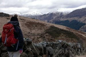 Girl standing beside a dry stone wall looking across to the snow topped hills