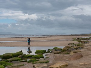 Girl walking on sandy beach with green moss covered rocks