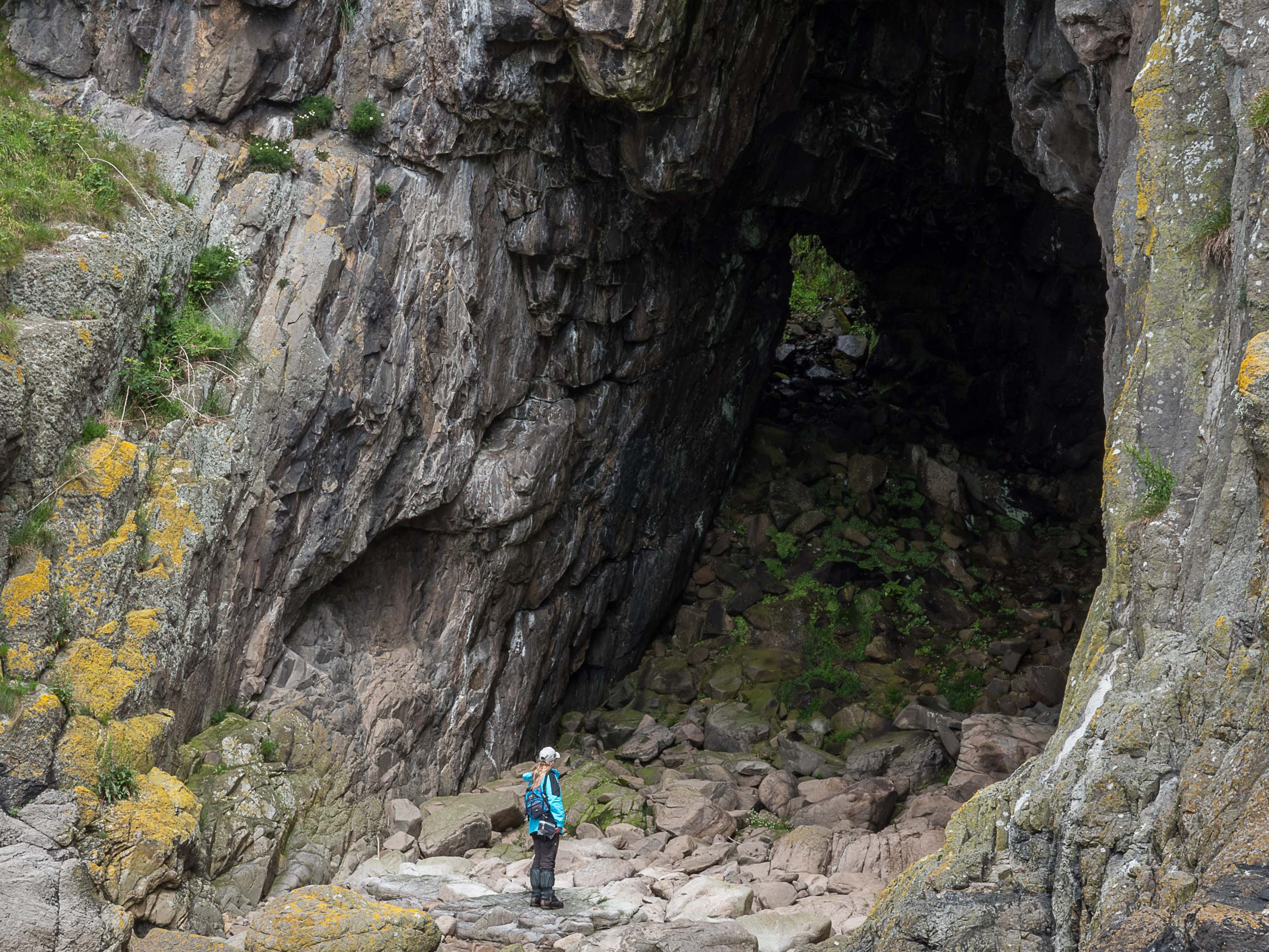 Girl standing at the entrance of high but shallow cave, known as the Black Cave