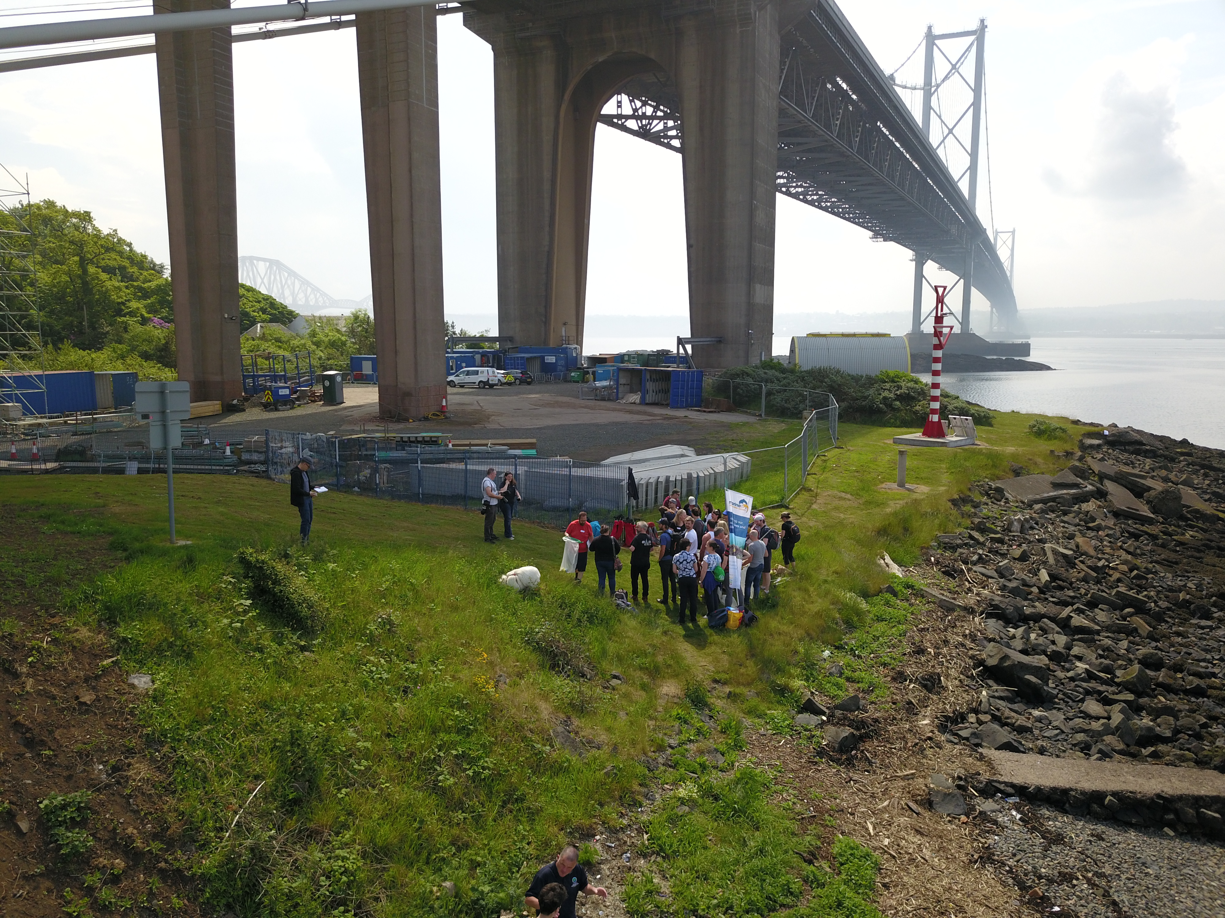 People gathered underneath a bridge and beside a rocky shore