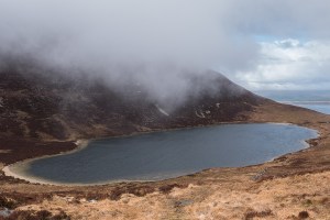 Mountain loch with a gravel beach from above and low cloud