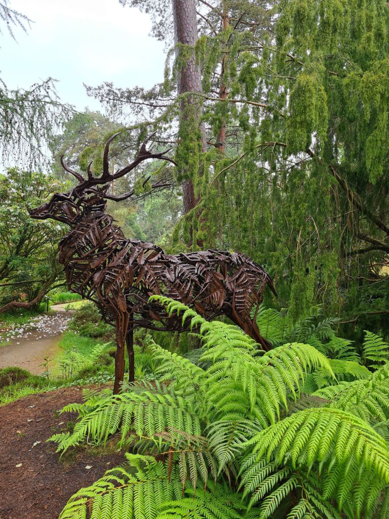Sculpture of a stag sitting amongst the trees and fer