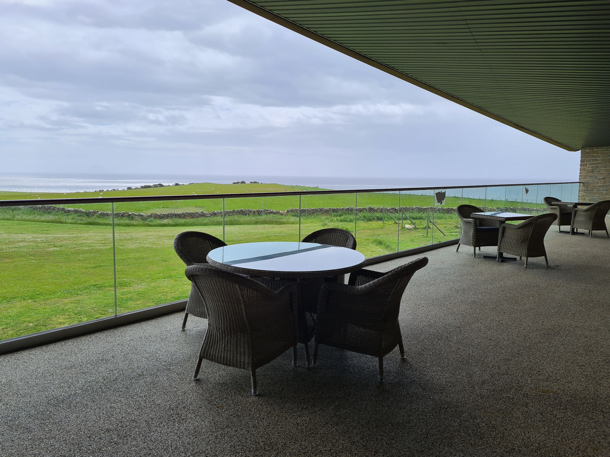 Outdoor balcony view of green fields, drystone wall, sheep and the ocean
