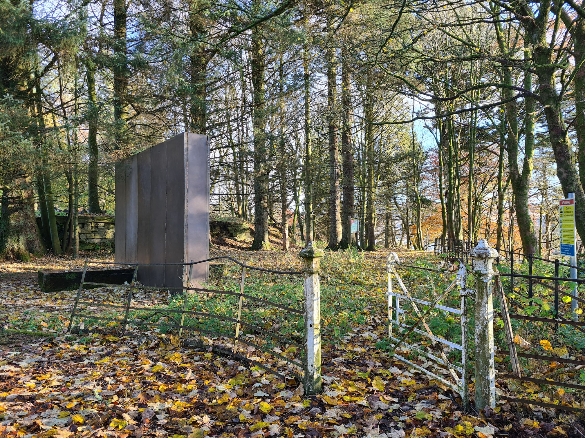 Old metal fence and gate leading into woodlands and a large rectangular sculpture