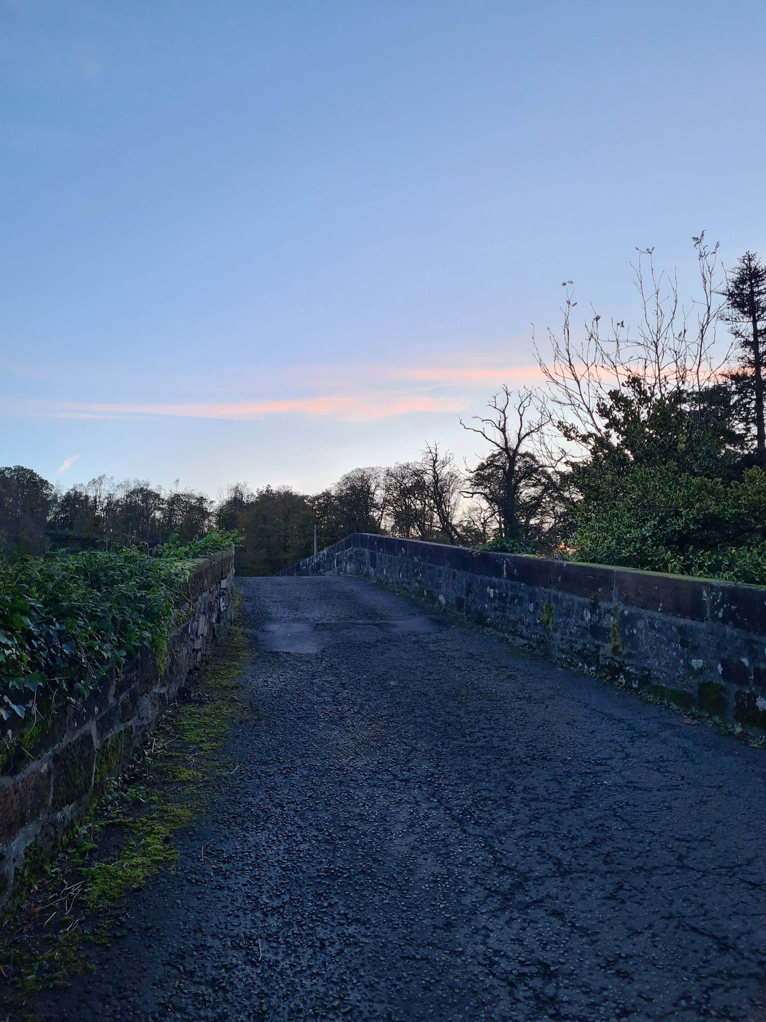 A narrow road across an old stone bridge at twilight