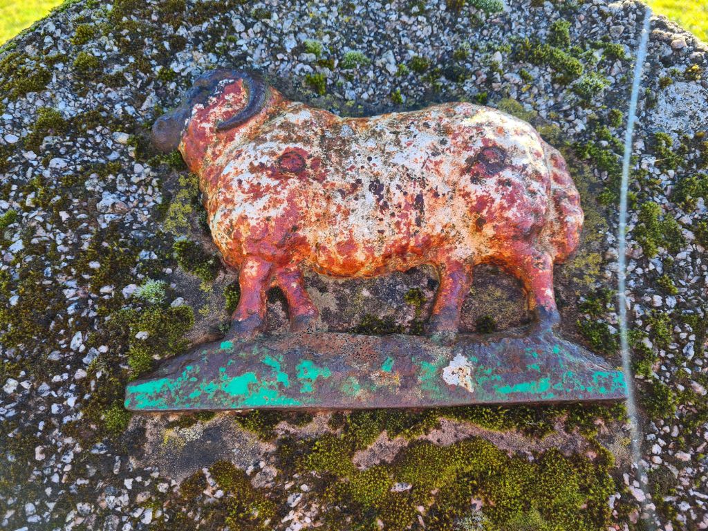 A metal carving of a sheep mounted to a stone memorial for Tibbie Pagan