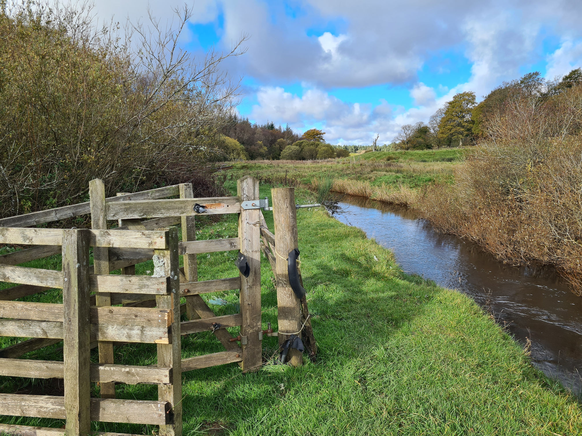 A wooden gate beside the river, but you can also walk around it as it's missing part of the fence