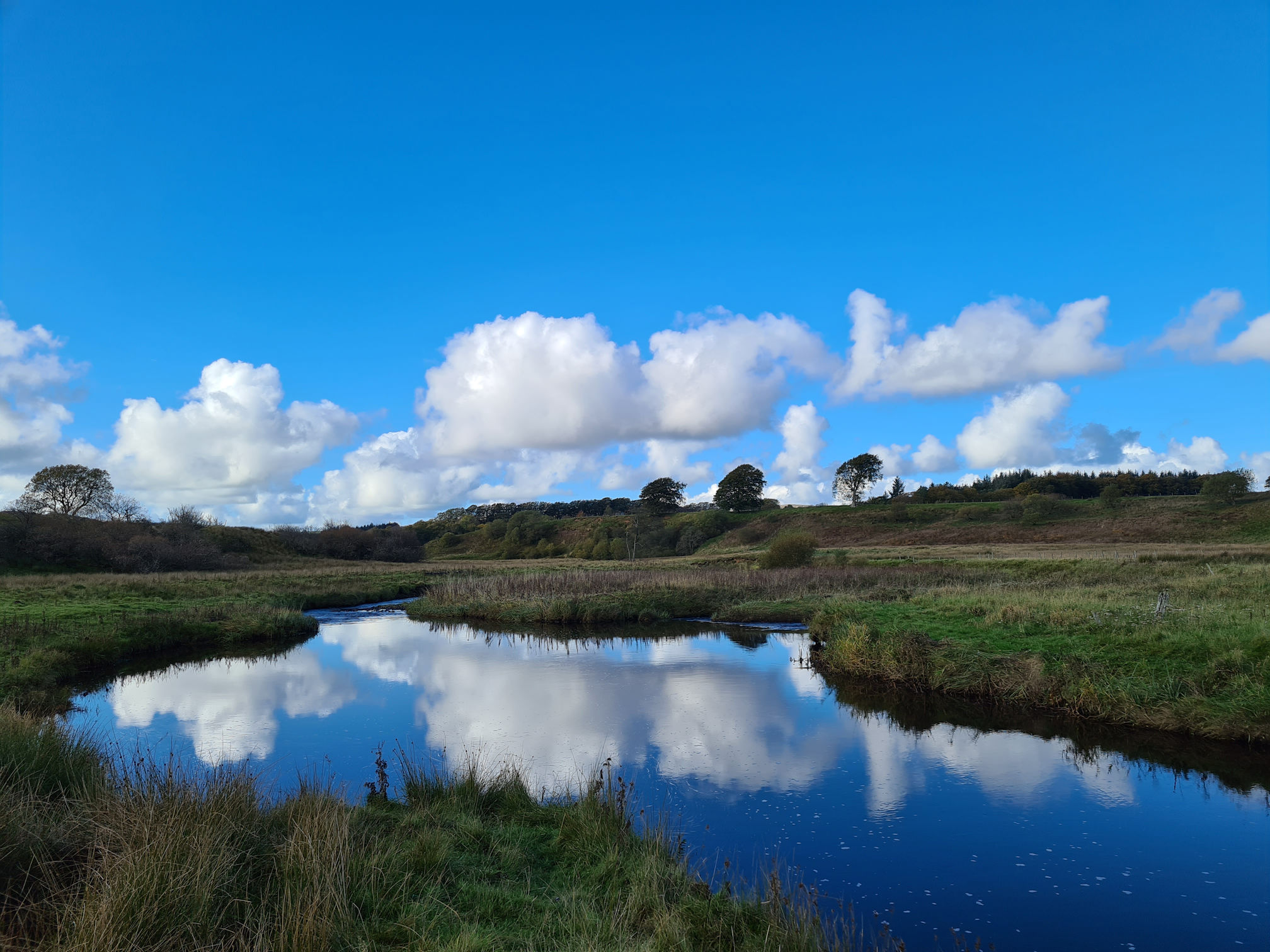 The bright blue sky and puffy white clouds are reflecting in the river like a water painting