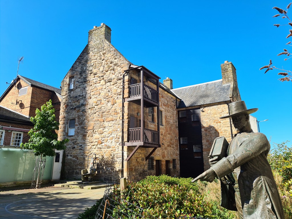 Statue portraying the Reverend William Adair, arm stretched out pointing, judging a woman to be a witch