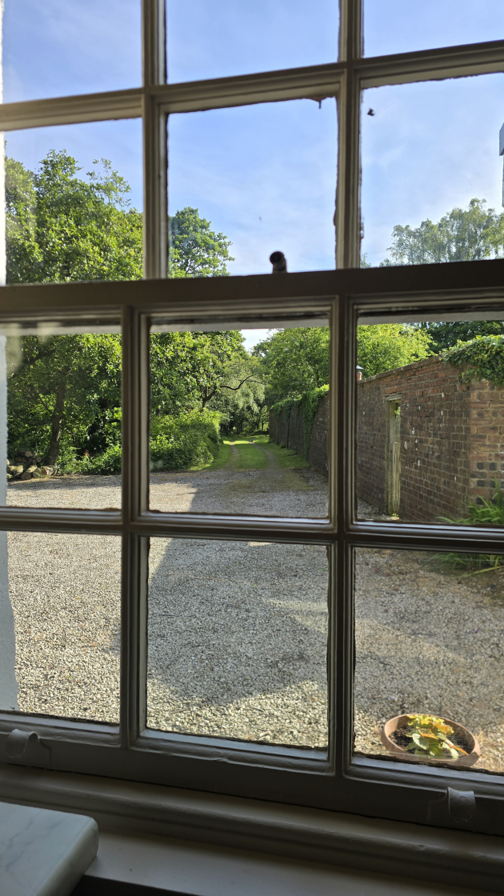 Square window panels with a view down a driveway and a walled garden on the right
