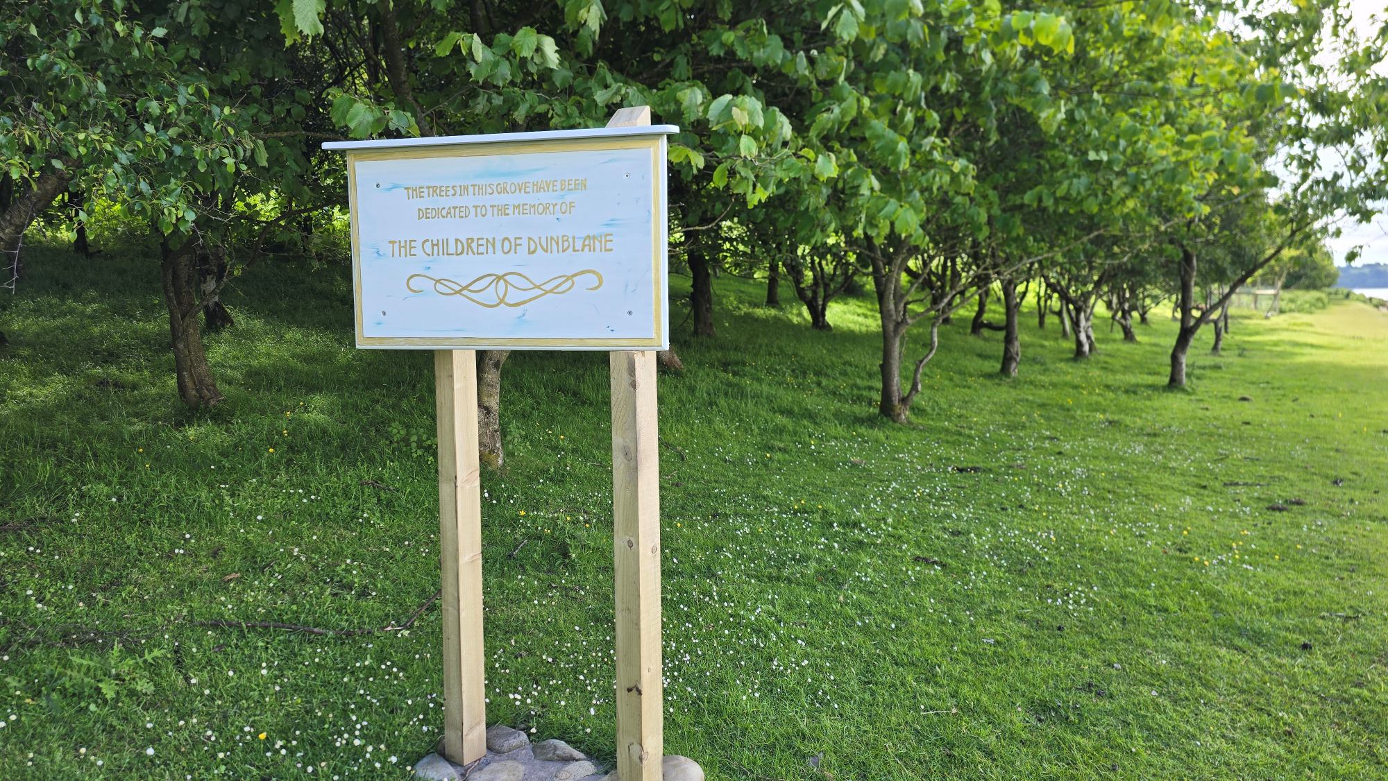 The sign says "The trees in this grove have been dedicated to the memory of the children of Dunblane"