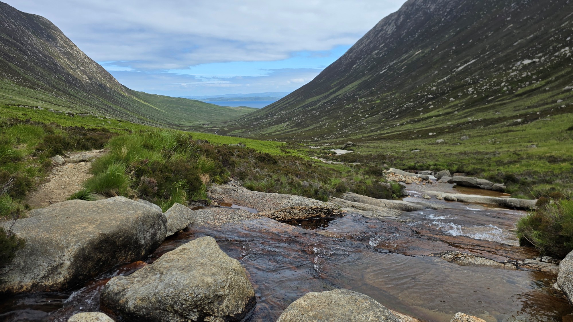 Boulders across as burn to help cross it and a view looking down a glen with steep mountain slopes on either side. You can see the sea at the end of the glen.