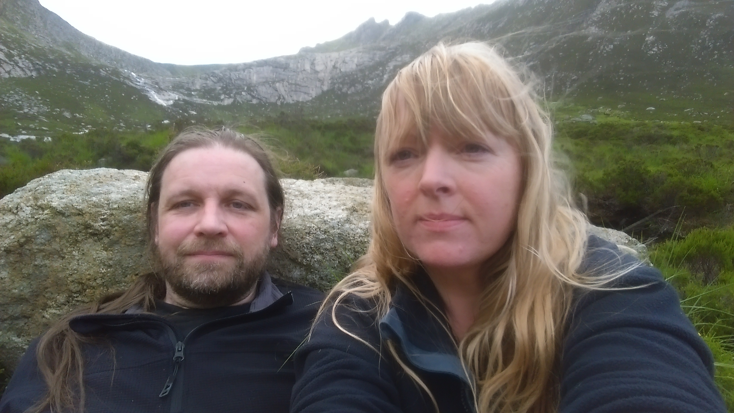 Young man and woman sitting beside a boulder in the mountains