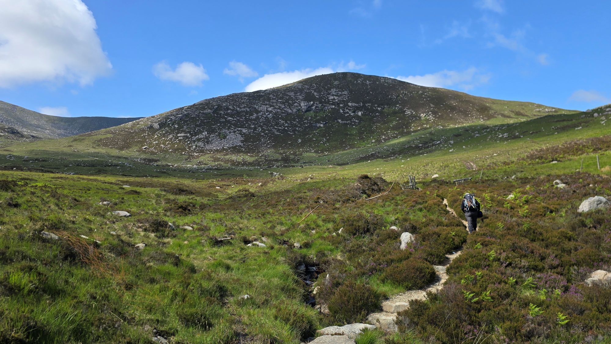Person walking on a path in the hills towards a broken fence