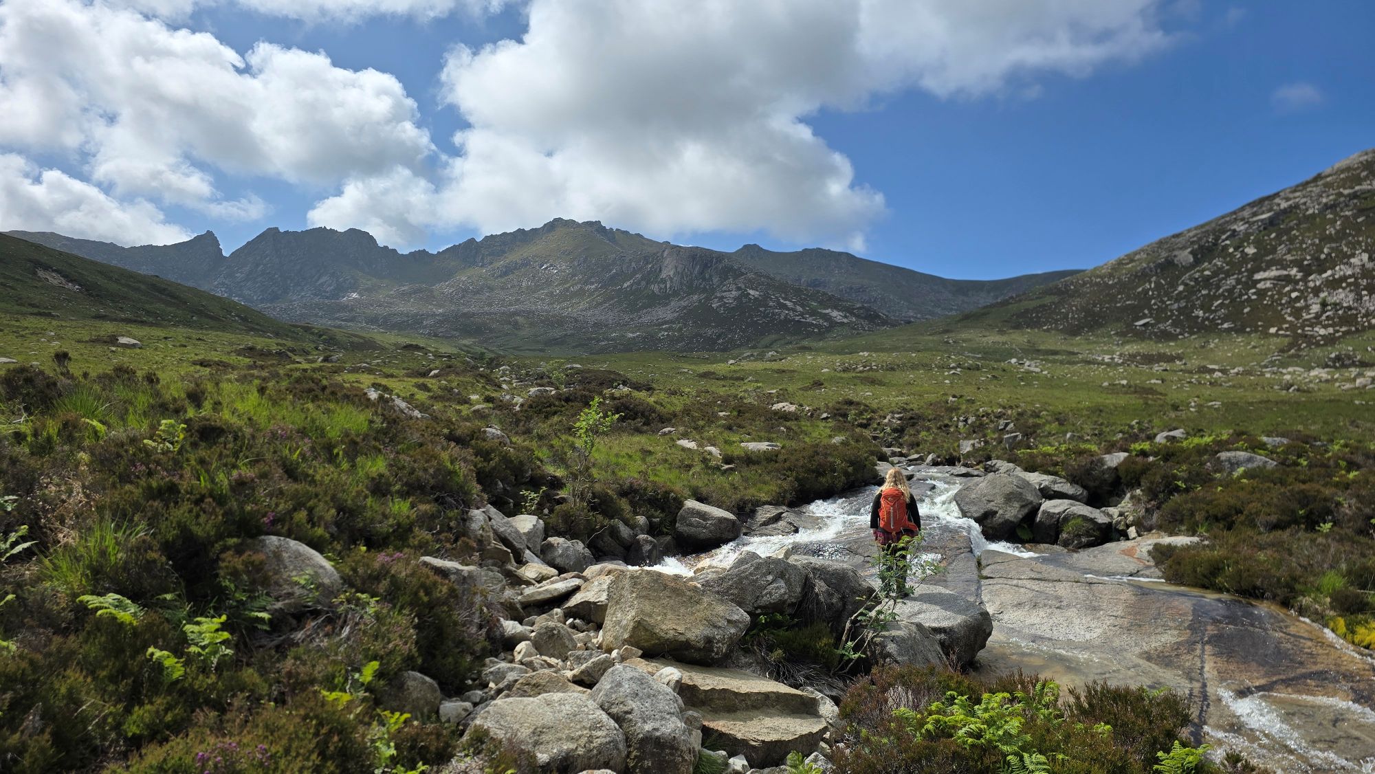 A girl standing on a flat boulder at North Glen Sannox Burn, looking towards the Arran mountains.