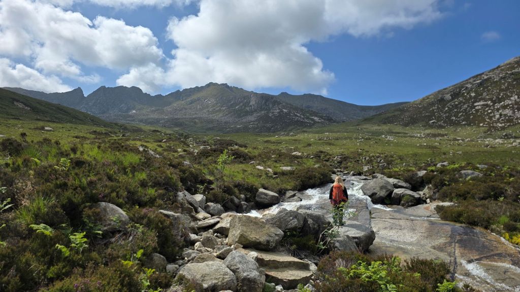 A girl standing on a flat boulder at North Glen Sannox Burn, looking towards the Arran mountains.