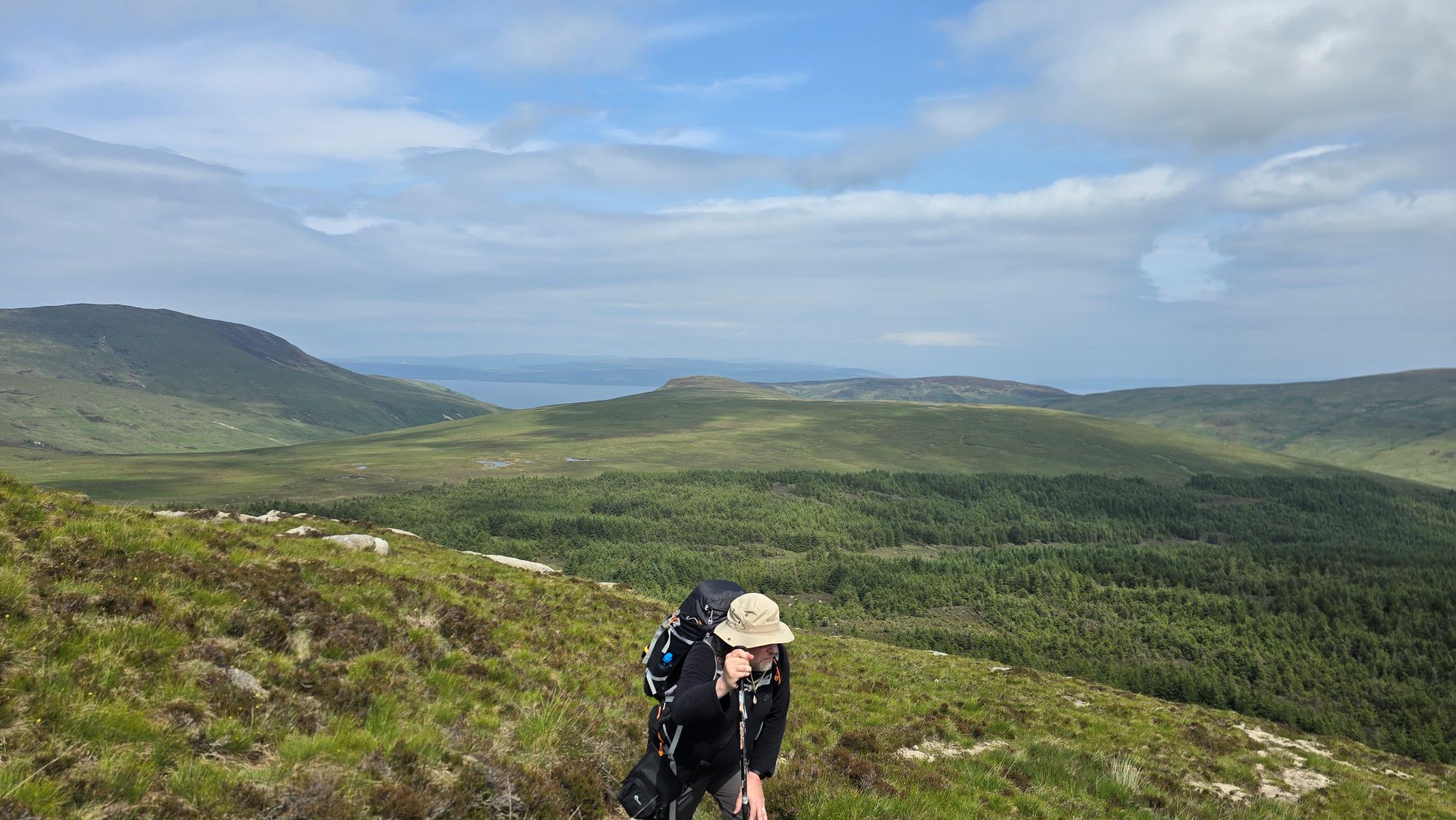 Man hiking up a hill with a heavy backpack