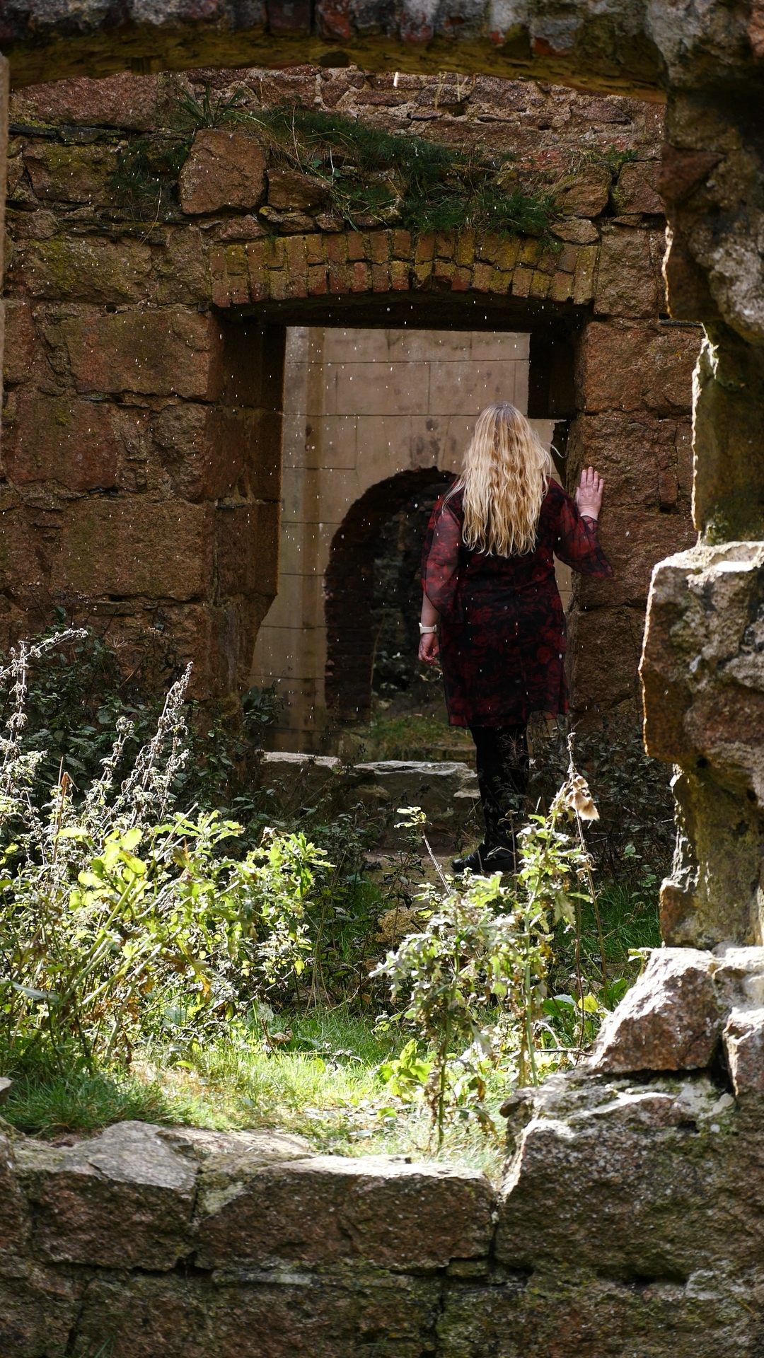 Girl in a red dress standing in castle ruins in the rain